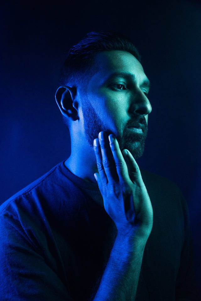 A beardsman's side profile in blue and green neon lighting applying product to their beard.